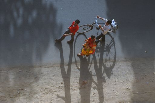 A view from above of a family walking on an empty road in the streets of Ahmedabad, India with a bike