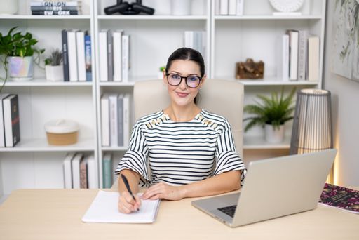 A Brunette adult female model working at computer in office wearing striped dress