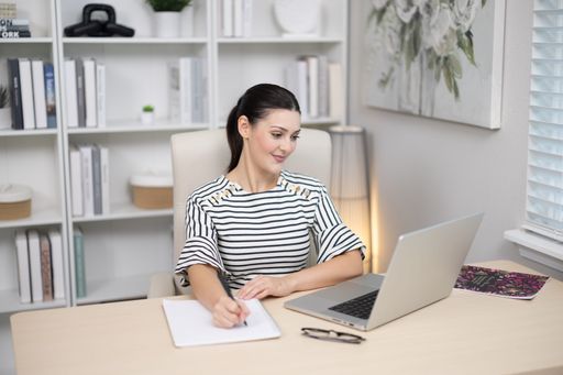 A Brunette adult female model working at computer in office wearing striped dress