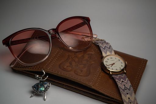 A closeup shot of a gold watch with sunglasses and a brown wallet on gray background