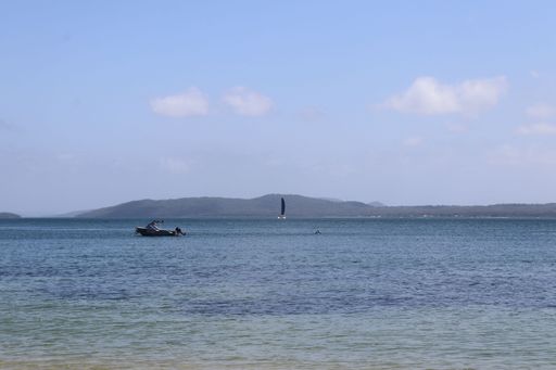 A tranquil seascape with a boat and sailboat on clear blue waters under a partly cloudy sky
