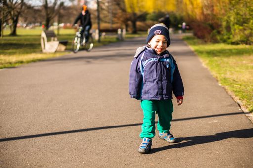 Happy small boy walking on a asphalt footpath in the Jan Pawla park on a sunny day.