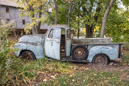 An old, rusted vintage truck sitting in the woods on a sunny autumn day