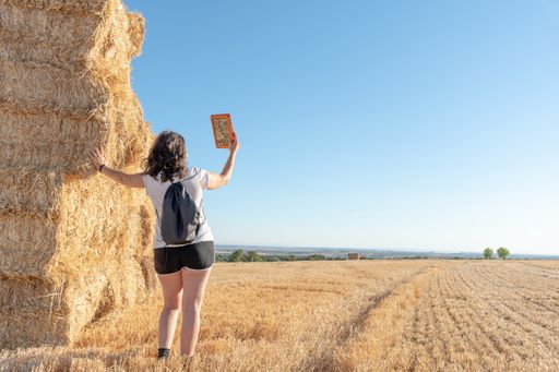 A scenic view of a middle-aged brunette Latina woman using a tablet while standing beside a straw bale