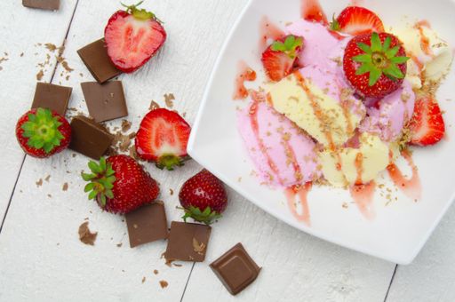 A top view of ice cream with strawberries and chocolate on a white wooden table