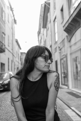An attractive youthful Hispanic female in sunglasses sitting on a chair in the middle of a street