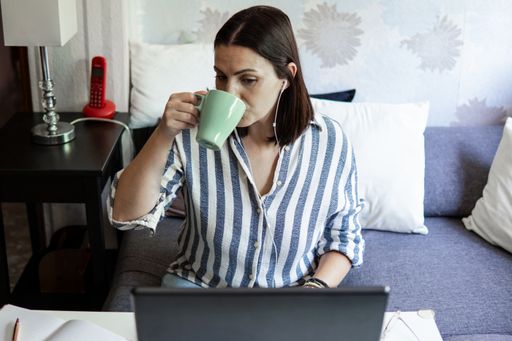 Caucasian white young woman working from home with laptop, doing video conference with headphones drinking coffe from a cup, with copy space