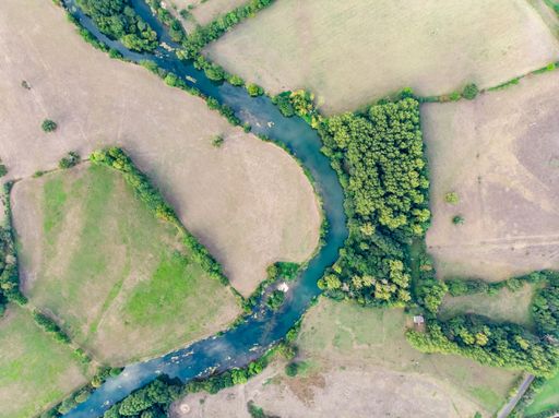 An aerial shot of a curve river through agricultural fields in the countryside