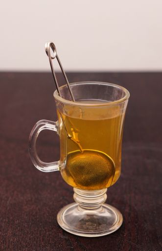 A vertical shot of a metal tea infuser inside a glass of tea