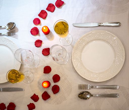 Glasses and bottle of wine with red rose petals on the table- concept for Valentine' day dinner with candle light in a restaurant.