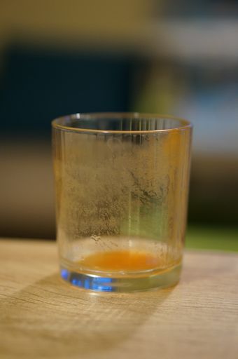 A vertical closeup shot of a dirty glass on a wooden surface with a blurred background