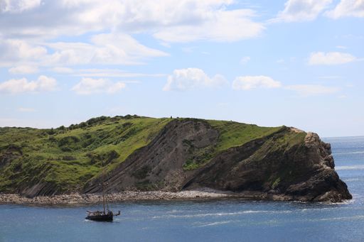 A scenic view of Lulworth Cove in Dorset, England with boats anchored in the clear blue water and lush green hills in the background