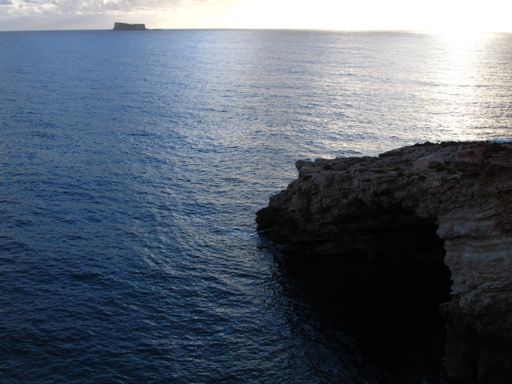 A sunset over the ocean with the islet of Filfla in Malta on a cloudy day
