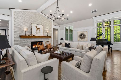 A modern living room with white furniture, brick fireplace, and large windows with a grand piano