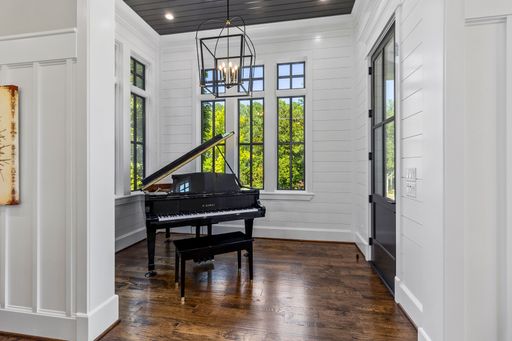 A bright and elegant music room with a grand piano, large windows, and hardwood floors