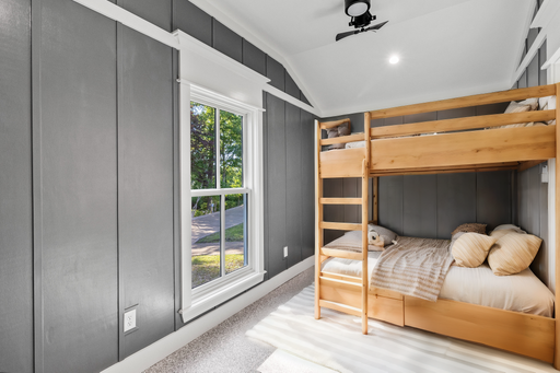 A modern cozy bedroom with wooden bunk beds, grey walls, and a large window letting in natural light