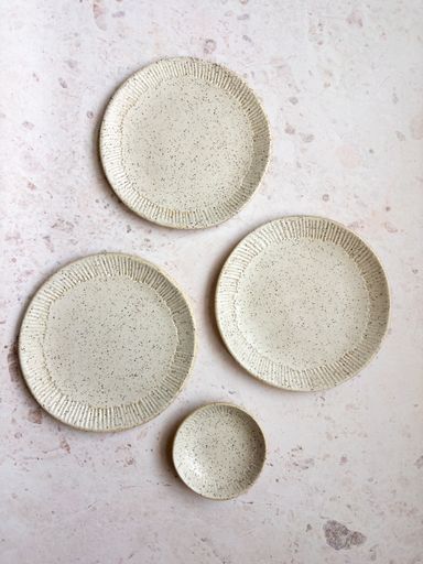 A set of four ceramic plates with a speckled design arranged on a light marble surface
