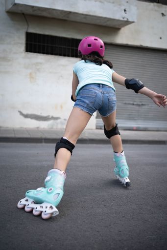 A girl in a pink helmet is skating on the street wearing knee pads and elbow pads