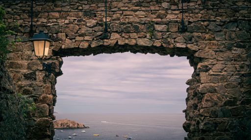 A scenic view of the sea through an ancient stone archway with a lantern