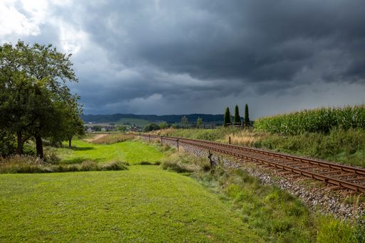 A scenic railway track passing through lush green fields under a dramatic cloudy sky