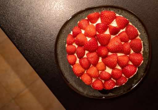 Top view of a strawberry cake on a dark plate placed on a textured surface