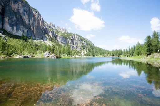 A stunning mountain landscape with a clear blue sky and a serene lake reflecting the surrounding cliffs and trees.