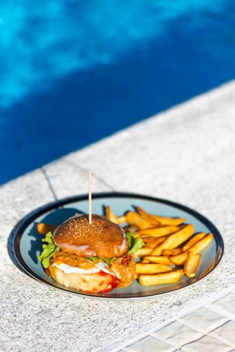 A vertical shot of a delicious hamburger and potato fry on a plate isolated by the poolside