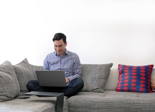 An Asian male sitting on the sofa and working with a laptop - working from home during the coronavirus pandemic