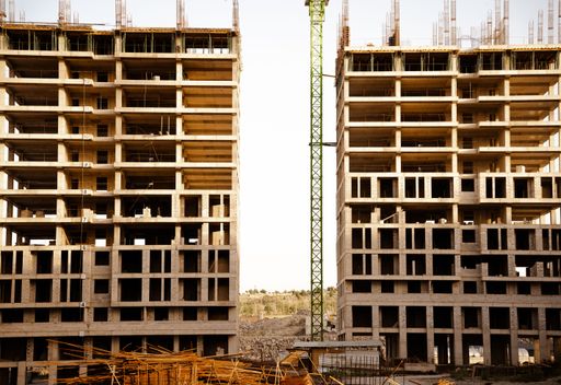 Two unfinished high-rise buildings under construction with a crane in between on a clear day