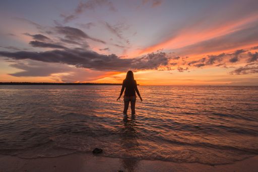 A silhouette of a woman standing on the shore at a beautiful sunset