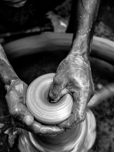 A monochrome shot of male hands making a clay vase on a pottery wheel