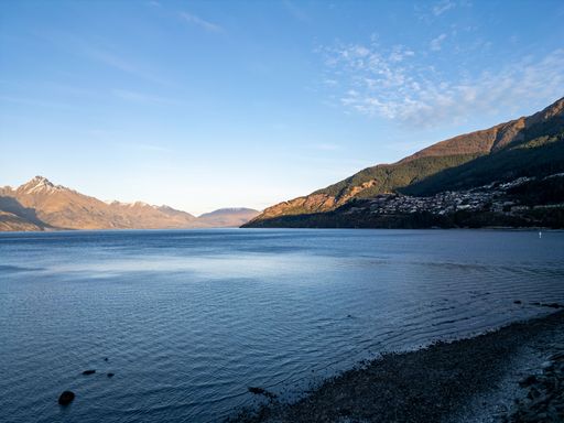 A serene view of Lake Wakatipu with surrounding mountains and clear blue sky in Queenstown, New Zealand.