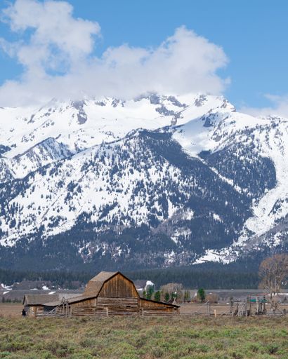 A rustic barn in front of snow-capped mountains under a clear blue sky in Grand Teton National Park.