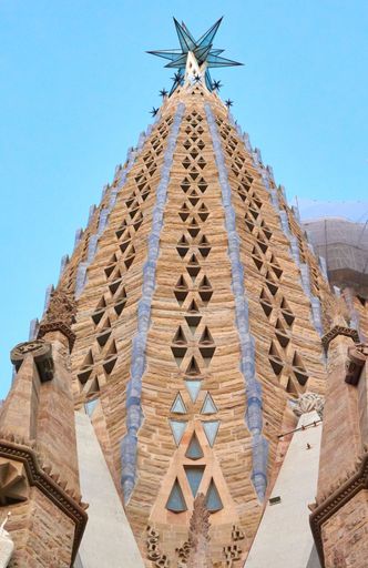 A vertical shot of the exterior details of Sagrada Familia Basilica Church with intricate historic decoration against blue sky in Barcelona, Spain