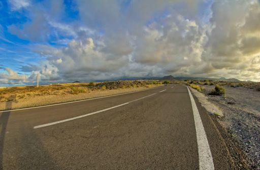 A shot of the asphalt-covered road surrounded by rocks and grass under a cloudy sky.