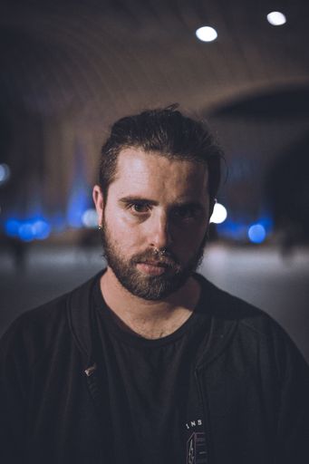 A vertical shot of a young male with a serious face wearing a black shirt with a blurred background