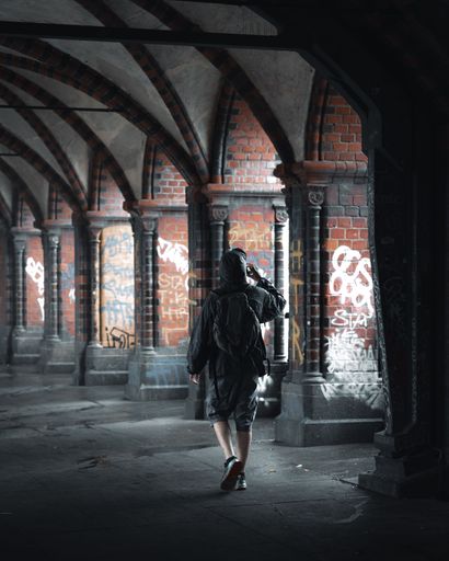 A person in a hooded jacket walking through a graffiti-covered brick archway in Berlin