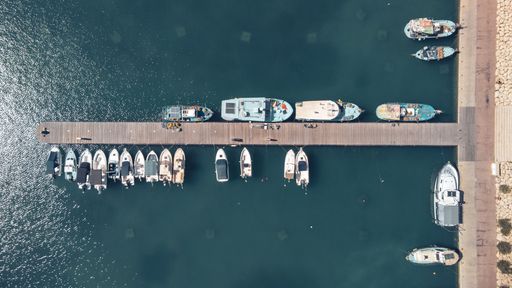 Aerial view of a marina with boats docked along a pier on a sunny day.