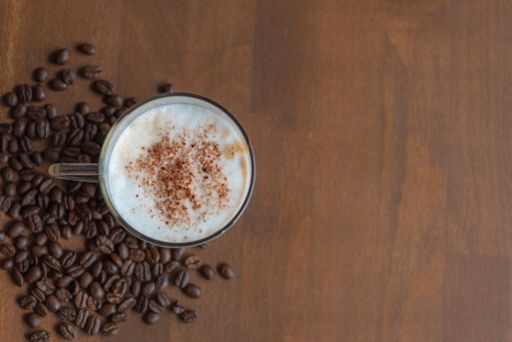 A top view closeup of glass with latte in it placed on a wooden table with coffee beans on it