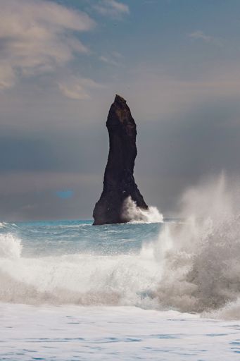 The view of crashing ocean waves and a cliff under a cloudy sky. Iceland