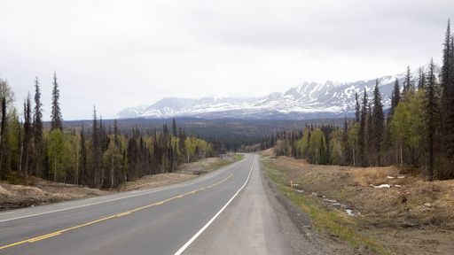 An empty winding highway through pine forest with snowy mountains in the background in winter