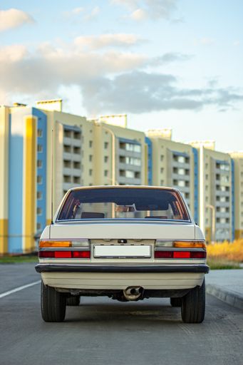 A behind shot of a white vintage classic car with buildings in the background