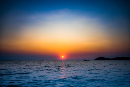 A serene sunset over the ocean with a boat silhouetted against the colorful sky