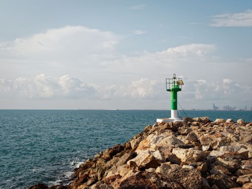 A green and white lighthouse on a breakwater of the beach of Valencia, with a blue sky and ocean in the background on a sunny day, Spain