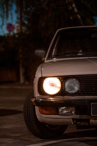 A beautiful shot of a white vintage classic car with round headlights in the street at night