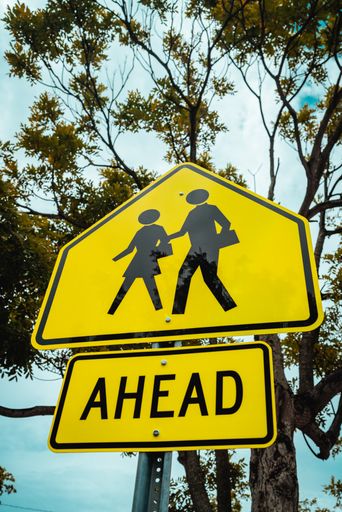 A vertical shot of a caution sign in yellow with persons symbols and text "Ahead"