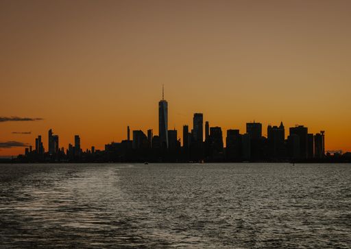 Silhouette of New York City skyline at sunset with orange sky and calm waters