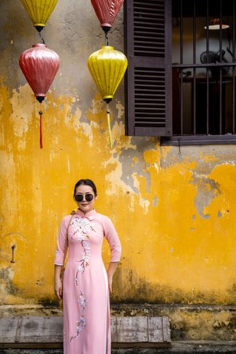 A young Asian female dressed in traditional clothes posing near a yellow weathered wall
