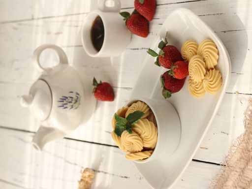 A vertical shot of meringue with strawberries, a cup of coffee, and a pot on a white wooden table