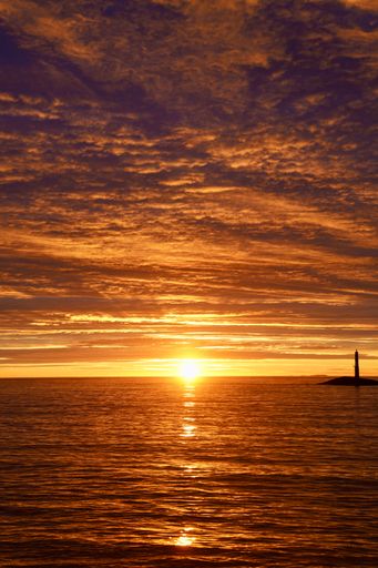 A stunning sunset over the ocean with a lighthouse silhouette